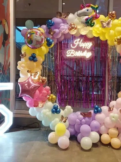 A unicorn and butterfly theme for a 5th birthday. This decoration features a circular balloon arch, a "Happy Birthday" neon sign, and a marquee number '5'.