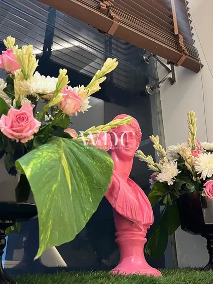 A pop of color and art. A bright pink bust statue is used as a quirky decor element, surrounded by fresh floral arrangements.