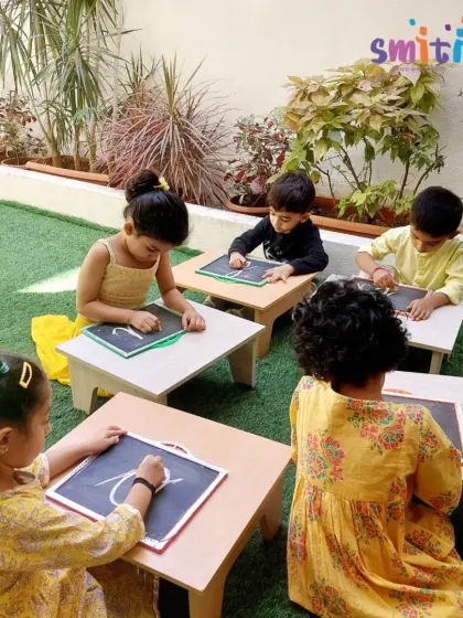 Children dressed in festive yellow sit outdoors, practicing their writing on slates. This activity combines cultural celebration with foundational literacy skills.
