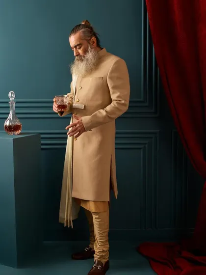 The full look of our beige draped sherwani, paired with a churidar. This outfit is perfect for a daytime wedding or a sophisticated evening event, offering a unique and memorable style.