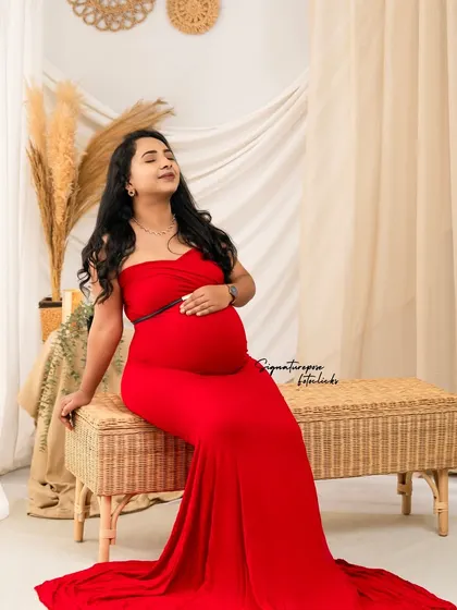 The vibrant red gown provides a stunning pop of color against the neutral tones of the boho wicker bench and backdrop.