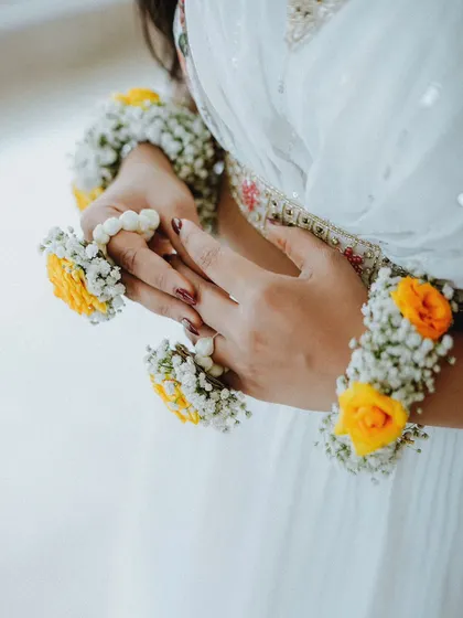 A close-up detail shot of the bride's hands, showing her beautiful floral bracelets and rings for the Haldi ceremony.