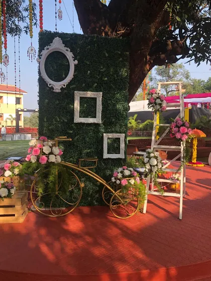 A rustic and charming photo booth for a Haldi ceremony. We used a green foliage wall with vintage frames, a decorative bicycle, and floral arrangements to create a unique selfie point.