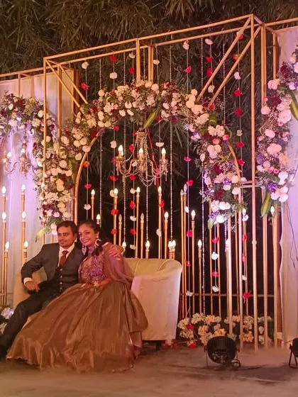 A romantic reception stage with a couple posing amidst smoke effects, framed by golden arches and floral arrangements.