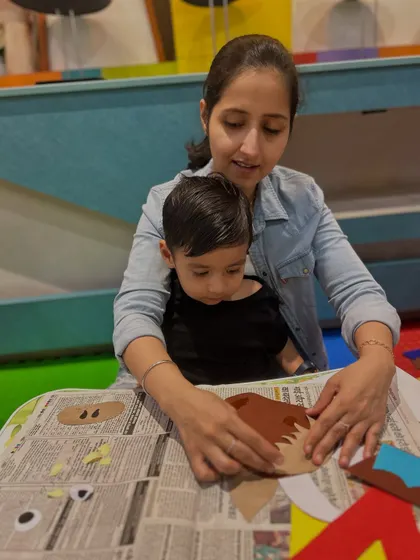 A mother and her son work on a paper yak craft, carefully placing the pieces together. This activity helps with recognizing animal shapes and parts.