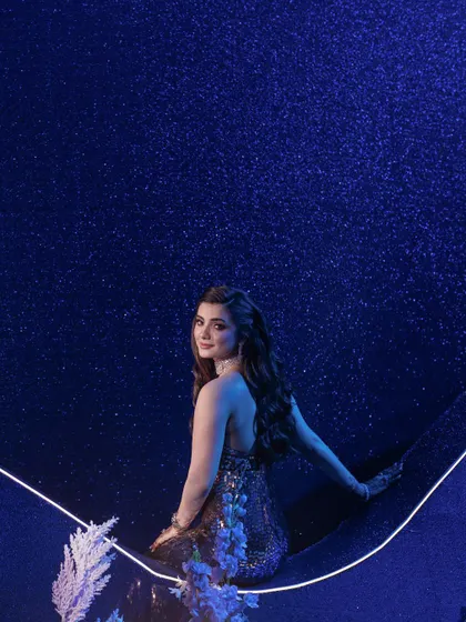 A beautiful portrait moment for the bride, seated against a deep blue, sparkling backdrop that mimics a starry night sky, enhanced by a clean, curved line of light.