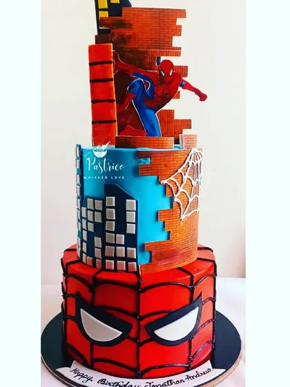 A dynamic three-tiered Spiderman cake, designed to look like the superhero is scaling a city building.