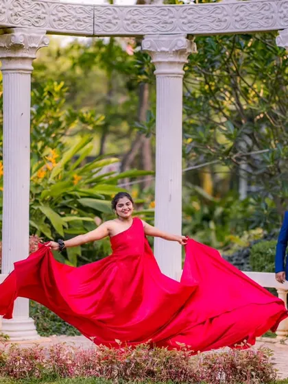 A joyful, twirling motion captured in the garden. The bride-to-be's red gown flows around her, creating a beautiful sense of movement and happiness in this pre-wedding shot.