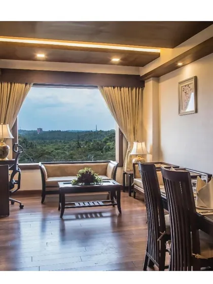 A view from a hotel suite in Calicut, overlooking a lush green landscape. The interior is appointed with classic wooden furniture and warm lighting to create a serene and comfortable guest experience.