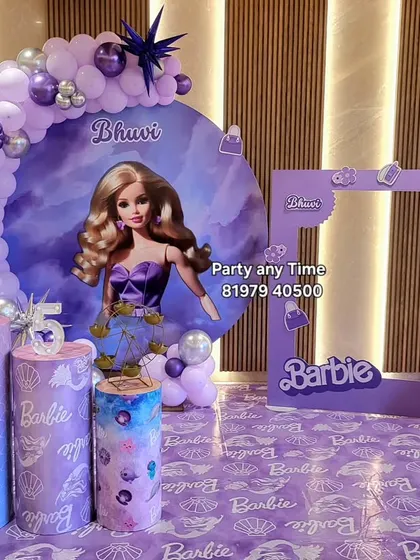 A stylish Barbie theme in purple, with a custom backdrop, a balloon arch, themed plinths, and a life-size Barbie photo frame prop.