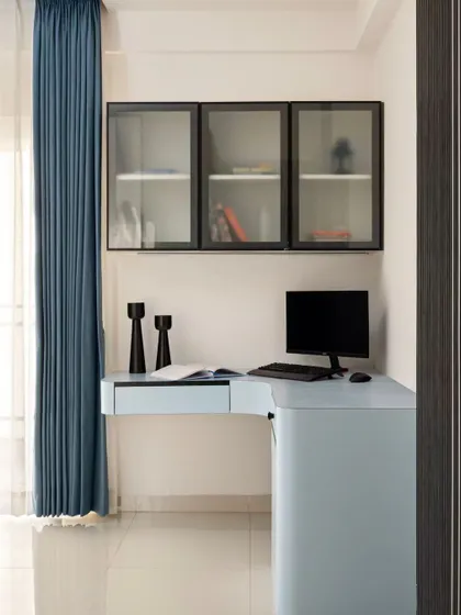 The son's study area in the same home is designed with a cool powder blue desk and black-framed overhead cabinets. It's a clean, modern, and functional workspace.