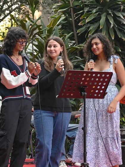 Three students singing into microphones at an outdoor stage during the Mela. We provide a platform for young talent to shine at our community gatherings.