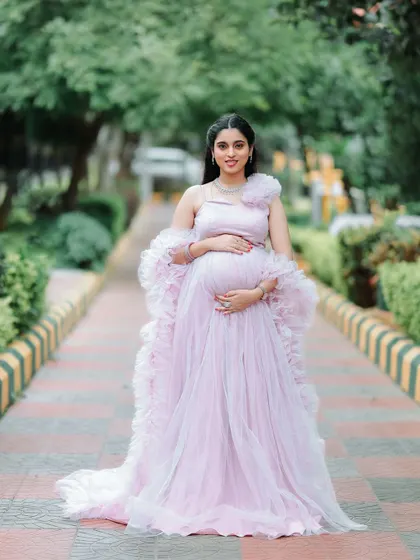 This mom-to-be looks absolutely stunning, cradling her baby bump. The one-shoulder design with a floral accent adds a unique touch to this popular pink maternity gown.