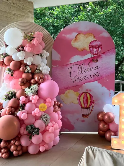 Ellora turns one! This beautiful first birthday setup on a balcony used shades of pink and rose gold balloons, a custom-printed backdrop with hot air balloons, and a light-up number '1'.