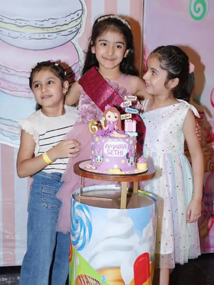 The birthday girl and her friends pose with her beautiful, personalized cake at her Candyland-themed party.