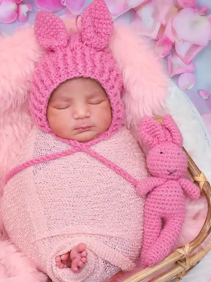 This baby girl looks adorable in a pink knitted bunny hat, swaddled cozily with her matching pink bunny toy.