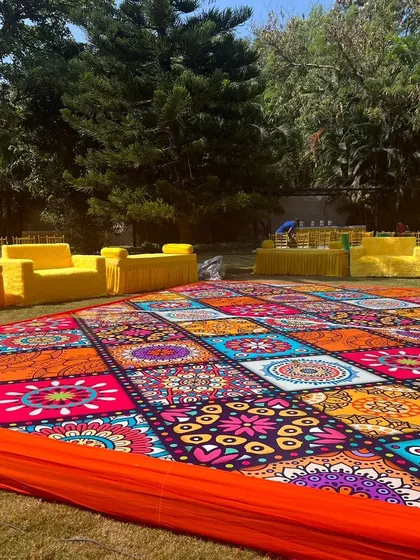 A fun and colorful outdoor Haldi ceremony in progress. I used a vibrant, mandala-patterned floor covering and bright yellow seating to create a joyful and festive environment perfect for the occasion.
