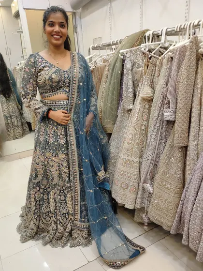 A happy client in our store trying on a grey-blue lehenga with heavy embroidery.