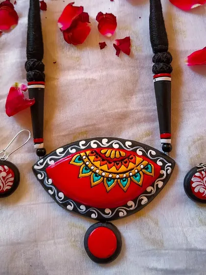 An artistic terracotta necklace with an eye-catching, fish-eye shape, combining mandala and alpona art in a red, black, and white palette.