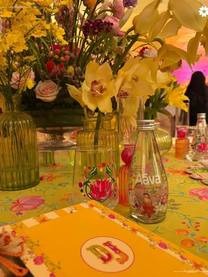 A vibrant tablescape from the Adani Mehendi, celebrating India's street food culture. The decor, with its bright yellow and floral motifs, custom water bottles, and colorful glassware, set a joyful and informal tone for the daytime celebration.