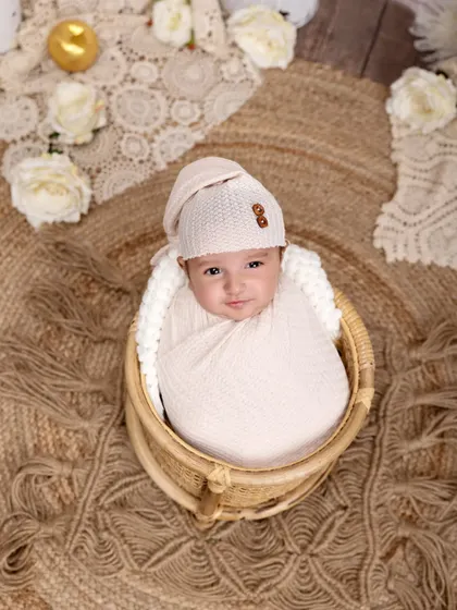 A sweet smile from a swaddled newborn in a wicker basket. The overhead angle and rustic jute rug create a warm and inviting composition.