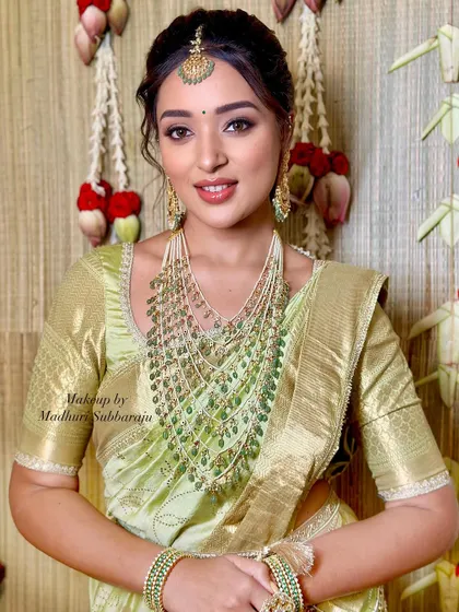 A portrait of the bride, her makeup perfectly complementing the unique green saree and layered emerald necklace.