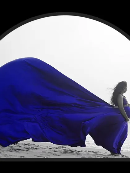 A dramatic shot of our blue flying gown against the sea, a popular choice for beach maternity photoshoots.
