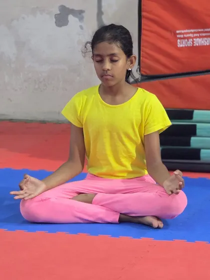 A young gymnast sits in a meditative pose, finding her focus. These moments of mindfulness help improve concentration during challenging drills and routines.