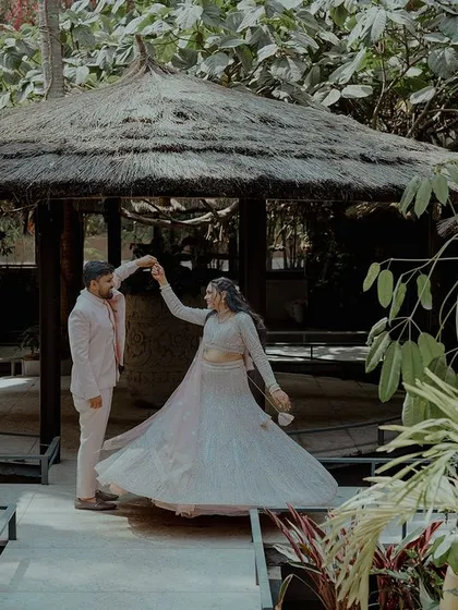 A couple shares a dance in a beautiful, rustic outdoor venue. The bride's twirling lehenga creates a sense of movement and joy.