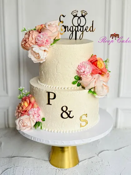 A masterpiece of love and elegance for an engagement. This two-tier cake is beautifully adorned with delicate flowers, a subtle stencil texture, and personalized with the couple's names.