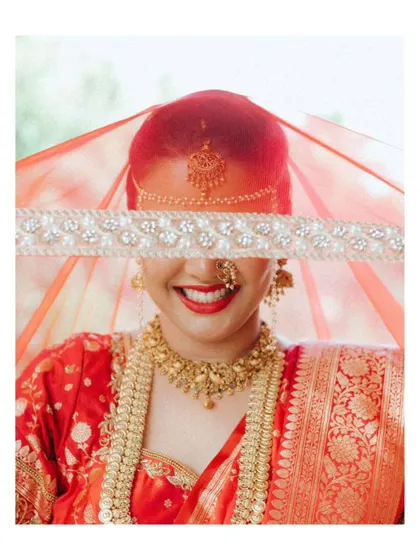 An artistic and joyful bridal portrait. The bride's smile is framed by her red veil, creating a vibrant and happy image.