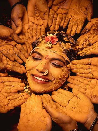 The pure joy of a Haldi ceremony. This photo captures the bride's beautiful smile as her loved ones surround her, their hands covered in turmeric, blessing her before her big day. It's a moment of tradition, love, and happiness.