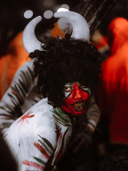 An intense close-up of a performer with striking red and white face paint and horns. The dramatic lighting and tight crop highlight the incredible artistry and character of the costume.