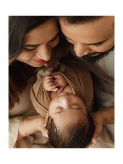 An overhead shot of parents looking down at their swaddled newborn, their hands creating a frame around the baby's head.