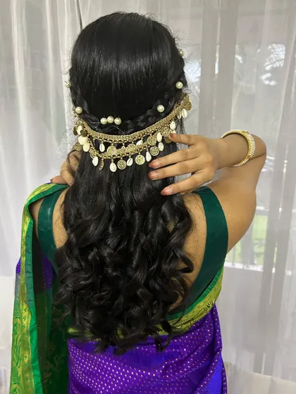A beautiful hairstyle for a Maharashtrian look, featuring soft curls and a traditional gold accessory with pearls and shells.