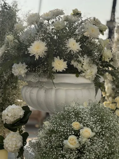 A detailed shot of a floral arrangement in a white urn, featuring a mix of chrysanthemums, roses, and baby's breath, showcasing the textures within the white-on-white theme.