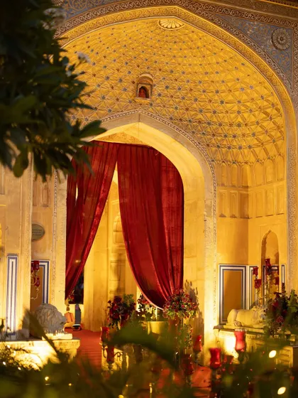The intricate, illuminated archways of Chomu Palace at night, with rich red curtains adding a touch of drama. The venue itself becomes a key character in the wedding's narrative.