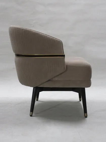 The side profile of this armchair reveals its unique, angular design and the beautiful contrast between the fabric and the dark wood legs with brass tips.