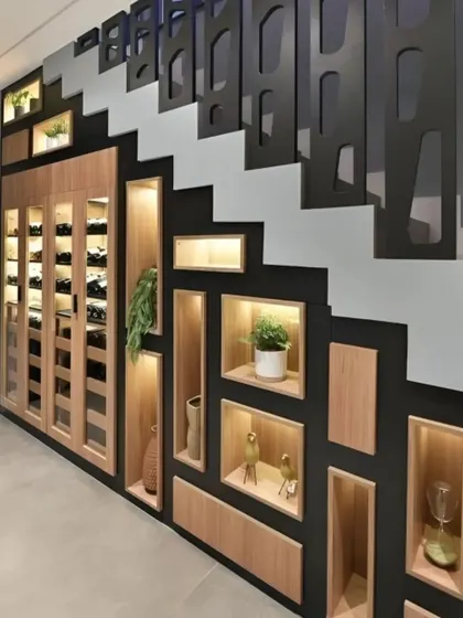 This design cleverly utilizes the space under a staircase for a decorative storage unit. The combination of a wine cabinet and illuminated display niches turns a typically unused area into a stunning feature.