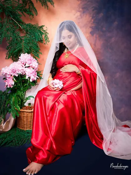 A wider shot of the veiled portrait, showing more of the beautiful red saree and the floral props, creating a complete, artistic scene.