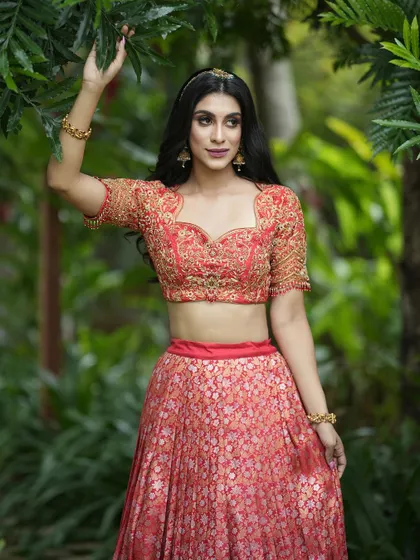 A close-up of the sweetheart neckline and intricate hand embroidery on the coral-red blouse. This design blends traditional motifs with a contemporary silhouette, perfect for a modern bride.