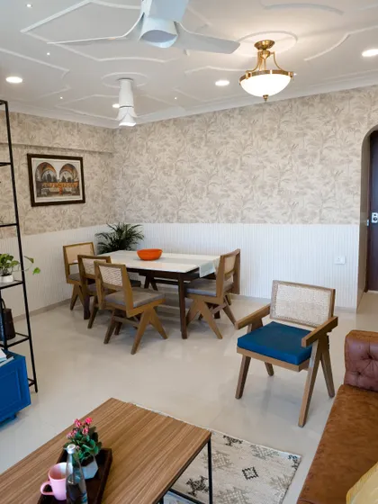 This living and dining area showcases a classic coffered ceiling design, adding a touch of traditional elegance to the space. The neutral wallpaper and wooden furniture create a warm, inviting feel.