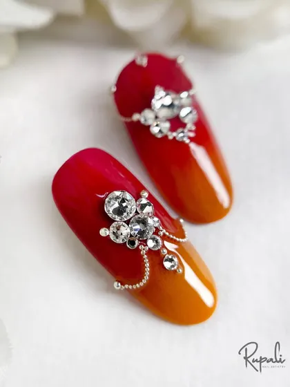 Two sample nails showcasing the intricate crystal work. The larger stones are surrounded by smaller ones and a delicate chain, creating a design with depth and dimension.