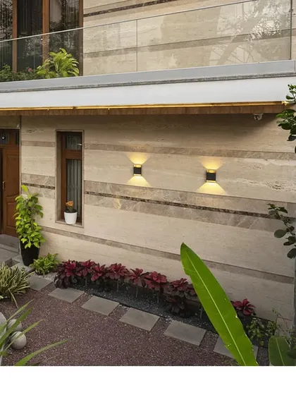 A close-up of a ground-floor garden space. The use of travertine cladding on the walls, combined with carefully selected plants and subtle wall lighting, creates a rich and textured outdoor nook.