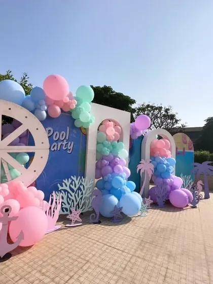 The full view of the poolside decoration, with multiple backdrops, a ship's wheel prop, and an anchor, all in a dreamy pastel color scheme.