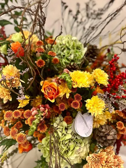 A close-up on the rich, autumnal colors of this artistic arrangement. The combination of yellow chrysanthemums, orange roses, and red ilex berries feels like a warm, painterly composition.