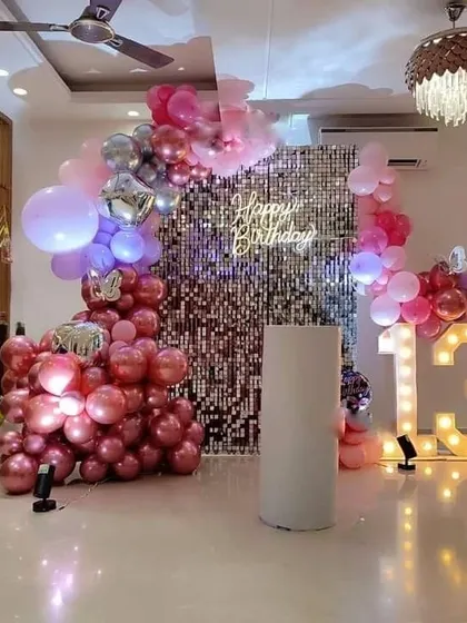 A trendy 13th birthday party with a rose gold shimmer wall, a 'Happy Birthday' neon sign, and a '13' marquee light, framed by a matching balloon garland.