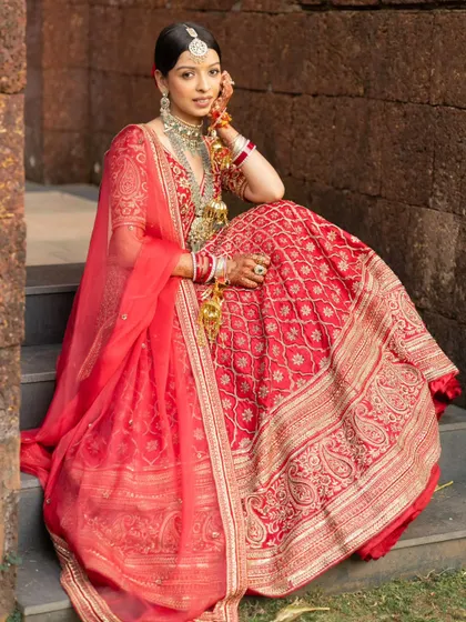A graceful seated portrait of the bride, showcasing the intricate details of her lehenga and jewelry.