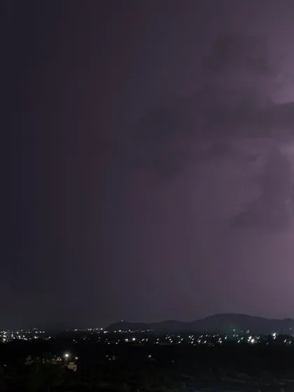 A bright, single bolt of lightning strikes down behind a hill on the outskirts of Pune.
