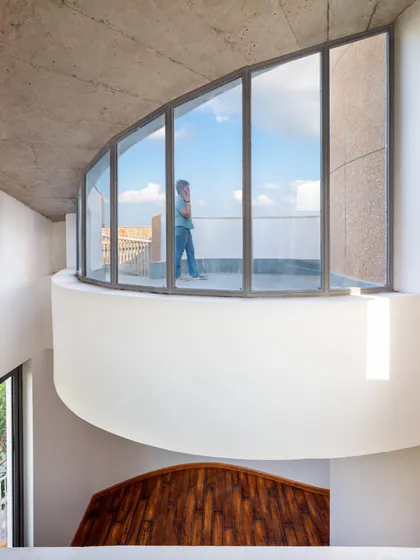 A curved balcony with floor-to-ceiling glass offers an expansive view, connecting the inhabitants with the sky and the surrounding environment.